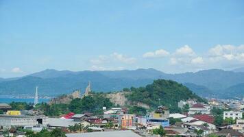 Landscape view of a residential building with mountains, blue sky, clouds, sea, and ocean in the background at Lampung. Copy space. Top view of city. Urbanization photo