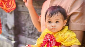 pequeño linda niña vistiendo amarillo balinés vestir con coño expresión en de papi regazo foto