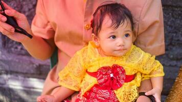 pequeño linda niña vistiendo amarillo balinés vestir con coño expresión en de papi regazo foto