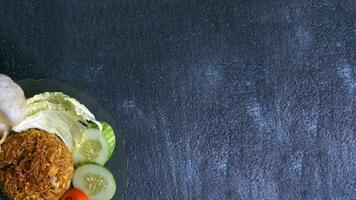 copy space of Nasi Goreng or fried rice, Indonesian street food, complemented cucumber, crackers, tomatoes, and cabbage sprinkled with fried onions with flat lay and dark background photo