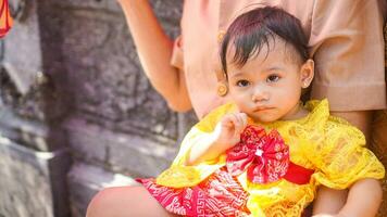 Little cute girl wearing yellow Balinese dress with fanny expression on daddy's lap photo