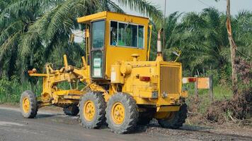 a yellow motor grader leveling stones and gravel for road repairs in Lampung. Behind view. photo