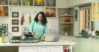 Happy woman watching video recipe on laptop while cooking  healthy lunch in kitchen using laptop