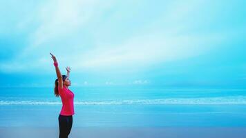 asiático mujer corriendo rutina de ejercicio trotar en el playa en el Mañana. ampliar el brazos relajarse. foto