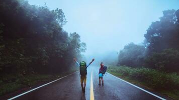 Lover asian man and asian women travel nature. Walk on the road route. traveling nature happily. Amid the mist rainy. photo