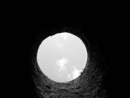 Stone well hole, old construction from inside, brick walls and blue sky background, fall down in the well concept photo