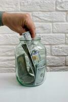 Mens hand taking out paper dollar banknote from glass jar photo