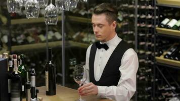 Sommelier examining wine at the wooden table with wine shelf in the background video