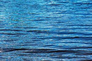 Fondo de textura de ondulación de agua. superficie de agua ondulada durante la puesta de sol, luz dorada reflejada en el agua. foto