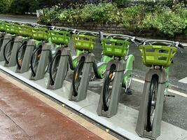 Bikes standing in row ready for rent, bicycle parking in city street close-up, healthy eco-friendly modern concept of urban structure, transport for leisure activity, going for work, summer rainy day photo