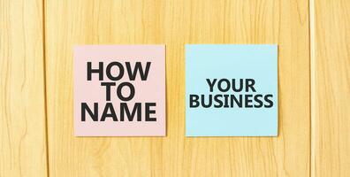 Inscription HOW TO NAME YOUR BUISINESS on pink and blue square sticky sticker on wooden wall photo