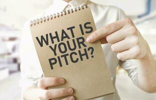 Text WHAT IS YOUR PITCH on brown paper notepad in businessman hands in office. Business concept photo