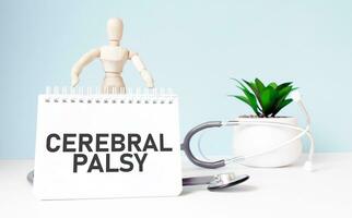 The text CEREBRAL PALSY is written on notepad and wood man toy near a stethoscope on a blue background. Medical concept photo