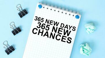 White notepad with text 365 new days 365 new chances and office tools on the blue background photo