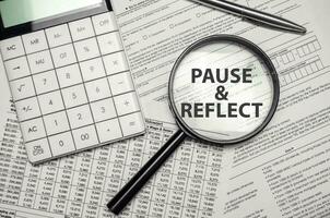 PAUSE AND REFLECT word on magnifying glass with calculator and documents photo