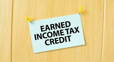 EARNED INCOME TAX CREDIT sign written on sticky note pinned on wooden wall photo
