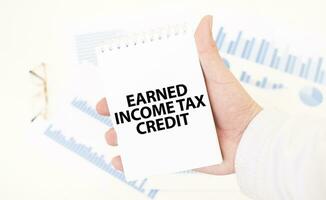Businessman holding a white notepad with text EARNED INCOME TAX CREDIT, business concept photo