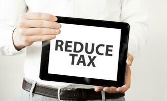 Text REDUCE TAX on tablet display in businessman hands on the white background. Business concept photo