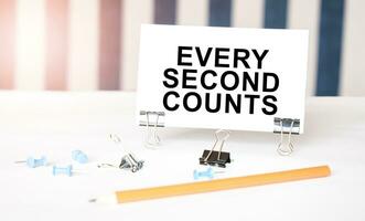 EVERY SECOND COUNTS sign on paper on white desk with office tools. Blue and white background photo