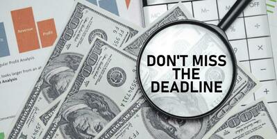 don't miss the deadline word on magnifying glass with dollars and charts photo