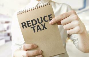 Text REDUCE TAX on brown paper notepad in businessman hands in office. Business concept photo