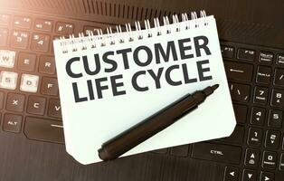 White paper sheet with text CUSTOMER LIFE CYCLE on the black laptop photo