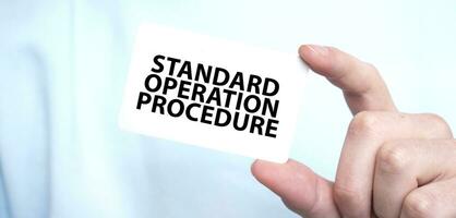 Man in blue sweatshirt holding a card with text STANDARD OPERATION PROCEDURE, business concept photo