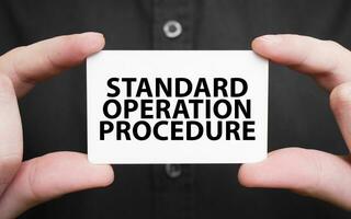 Businessman holding a card with text STANDARD OPERATION PROCEDURE, business concept photo