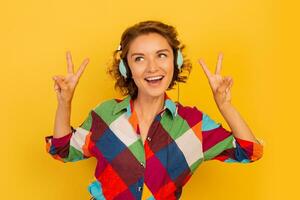 Happy woman with short hairstyle listenning music by earphones  and having fun over yellow background. photo