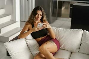 Pretty brunetre  woman sitting on cozy sofa  in stylish modern interior.  Wearing stylish sport clothes. photo