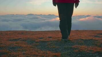 Woman is walking to the edge of mountain plateau above clouds. Legs shot. video