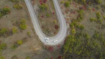Cars go on turn of serpentine mountain road. Aerial vertical top view video