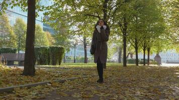 giovane bellissimo brunetta donna con arricciato salutare lungo capelli e borsetta è a piedi nel parco video