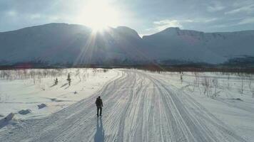 solitaire homme est randonnée dans montagnes dans ensoleillé hiver journée et en utilisant randonnée poteaux. aérien voir. drone est en orbite autour. le modèle se déplace loin. établissement tir. . video