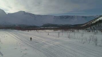 homme est randonnée dans montagnes dans ensoleillé hiver journée et en utilisant randonnée poteaux. aérien voir. drone est en orbite autour. établissement tir. lent mouvement.. video