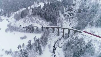 viadukt och tåg på vinter- dag i swiss alperna. snöar. schweiz. antenn se. Drönare flugor framåt- och nedåt video