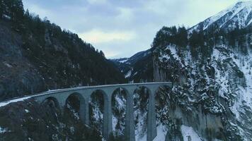 lixeiro viaduto com estrada de ferro às inverno dia. montanha desfiladeiro e rio. aéreo visualizar. suíço Alpes, Suíça. zangão moscas avançar, para cima, Câmera inclina baixa video