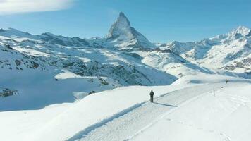 Blue Matterhorn Mountain and Standing Hiker in Winter Day. Swiss Alps, Switzerland. Low Level Flight Over Man. Aerial View. Drone Flies Forward video