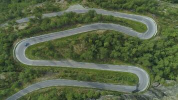 azul carro é indo em montanha enrolamento estrada dentro Noruega dentro verão dia. verde floresta. aéreo vertical Careca visualizar. zangão é ascendente video