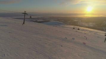 Menschen sind Skifahren und Snowboarden auf Ski Steigung mit Kabel Auto beim sonnig Winter Sonnenuntergang. Sonne im rahmen. Antenne Sicht. Drohne ist fliegend seitwärts. Festlegung Schuss.. video