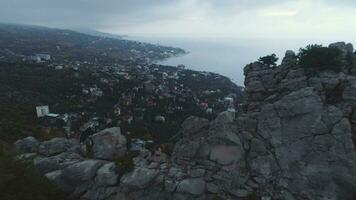 Woman is sitting on a rock and looking at the city on coastline. Aerial view video