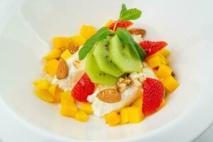 fruit salad with kiwi, strawberries, mango and nuts in a deep plate side view photo