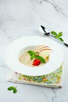 apple porridge with mint and strawberries in a white plate, side view photo