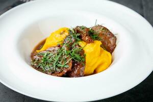 mashed potatoes with meat, sauce and herbs in a deep plate side view photo