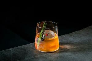 aromatic cocktail with a sprig of pine needles and round ice on a dark background, side view photo