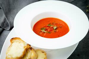 red tomato cream soup with herbs and toasted bread side view photo