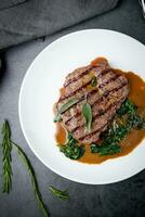 beef steak with gravy and herbs on a white plate top view photo