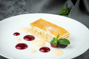 white sponge cake with drops of syrup, mint and wild berries on a round plate side veiw photo