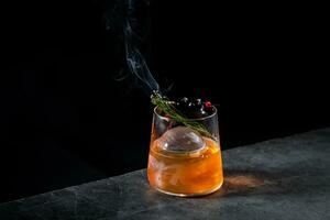 aromatic cocktail with a sprig of pine needles and round ice on a dark background, side view photo