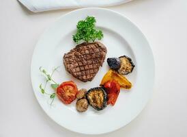 beef steak with grilled vegetables and herbs on a light background top view photo